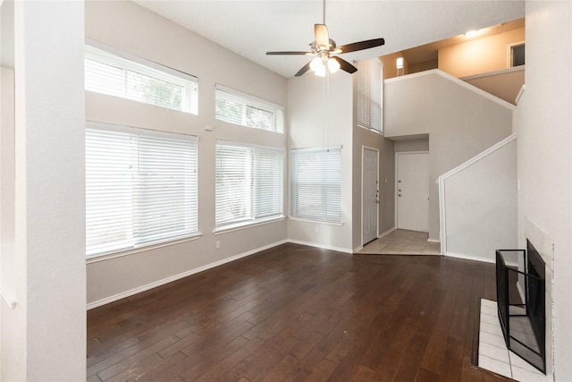 unfurnished living room featuring baseboards, a towering ceiling, a ceiling fan, and hardwood / wood-style flooring