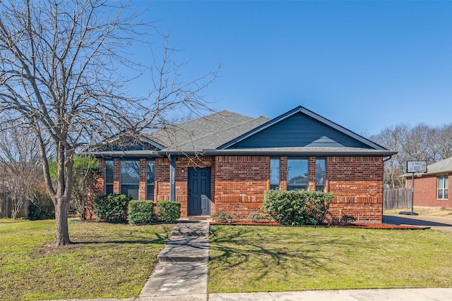 single story home with fence, brick siding, a front lawn, and a shingled roof