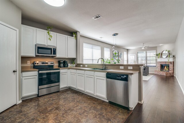 kitchen featuring a sink, open floor plan, appliances with stainless steel finishes, a peninsula, and white cabinets