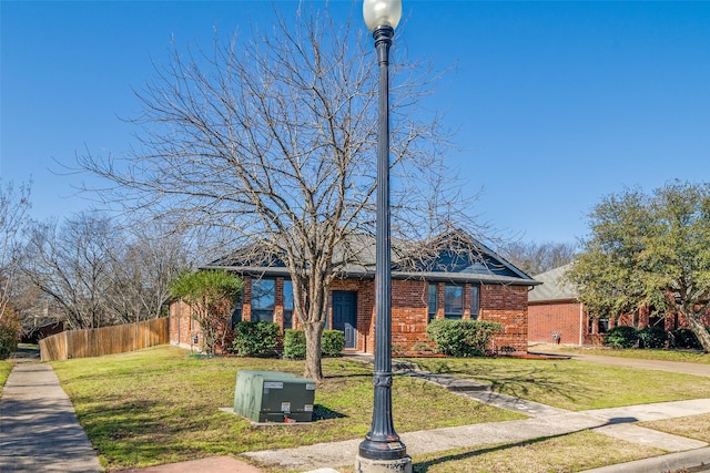 view of front of house featuring brick siding, a front lawn, and fence