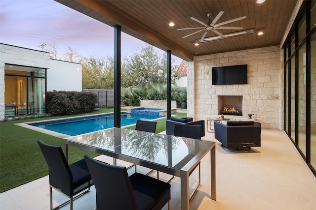 view of swimming pool with outdoor dining space, a ceiling fan, a patio, a fenced backyard, and an outdoor stone fireplace