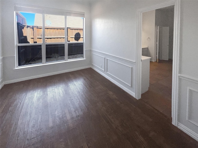 empty room featuring a decorative wall, wood finished floors, and wainscoting