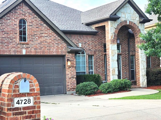 view of front of house with an attached garage, brick siding, stone siding, and a shingled roof