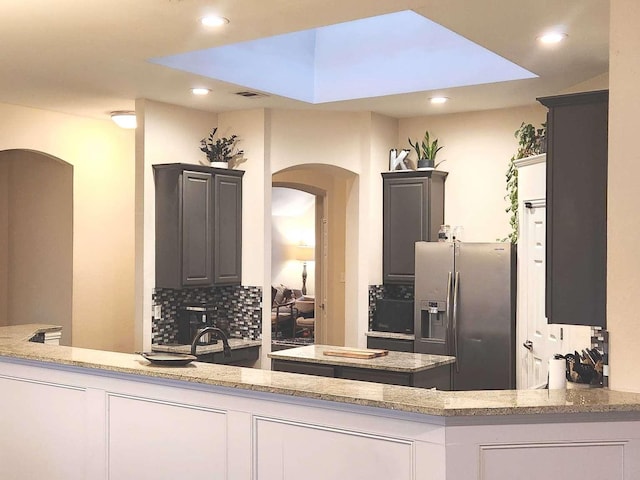 kitchen featuring decorative backsplash, stainless steel fridge, arched walkways, and light stone countertops