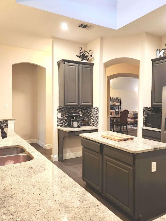 kitchen featuring tasteful backsplash, visible vents, light stone countertops, arched walkways, and a sink