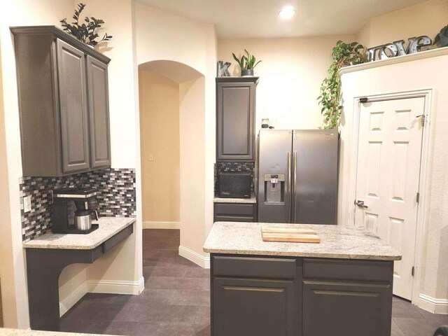 kitchen featuring light stone countertops, baseboards, arched walkways, stainless steel refrigerator with ice dispenser, and tasteful backsplash