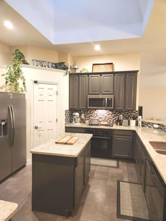 kitchen with light tile patterned floors, light stone countertops, a kitchen island, stainless steel appliances, and decorative backsplash