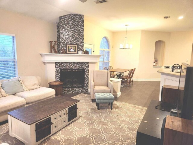 living room featuring a tiled fireplace, visible vents, arched walkways, and baseboards