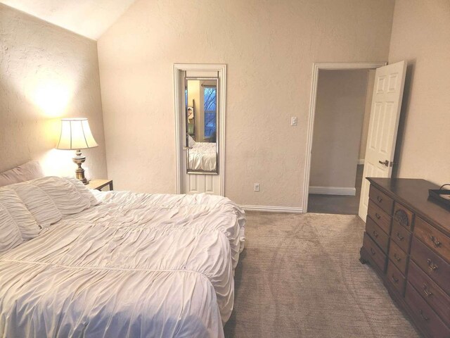 bedroom featuring vaulted ceiling, carpet flooring, a textured wall, and baseboards