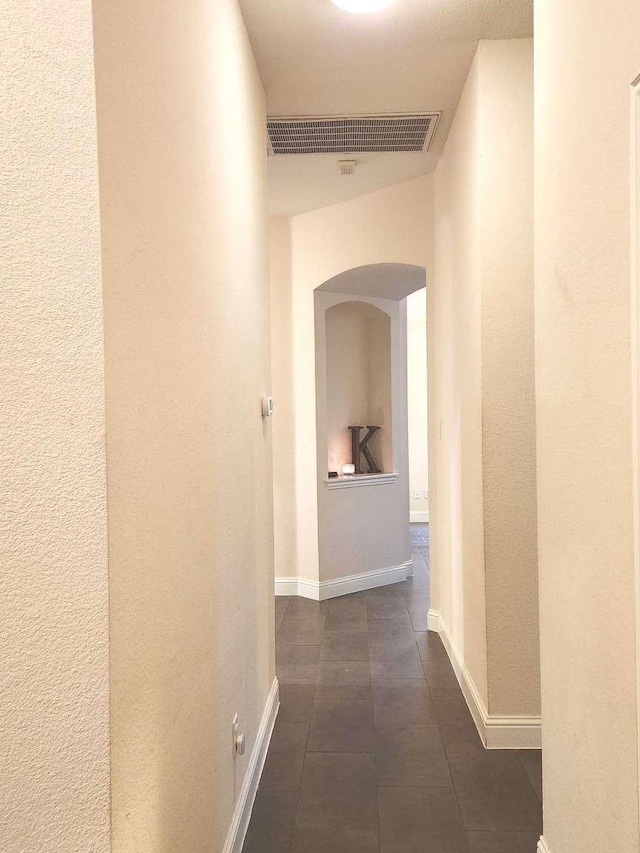 corridor with visible vents, arched walkways, baseboards, and dark tile patterned floors