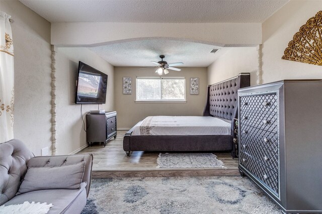 bedroom featuring a ceiling fan, visible vents, wood finished floors, arched walkways, and a textured ceiling