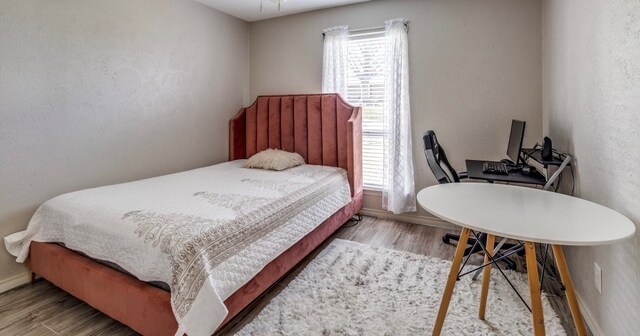 bedroom featuring a textured wall, baseboards, and wood finished floors