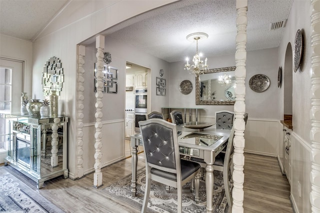 dining space with a wainscoted wall, arched walkways, a textured ceiling, a notable chandelier, and light wood-type flooring