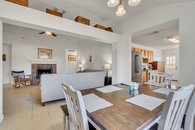 dining area with light tile patterned floors, visible vents, lofted ceiling, a fireplace, and ceiling fan