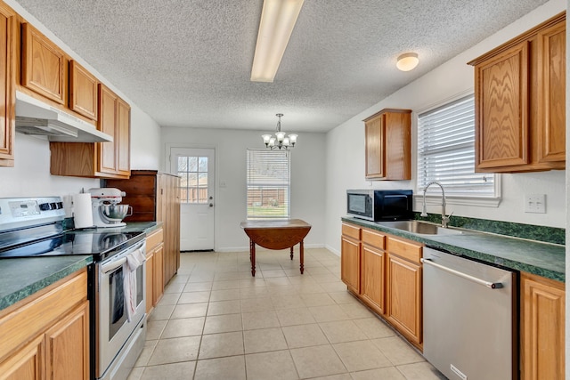 kitchen featuring a healthy amount of sunlight, a sink, stainless steel appliances, under cabinet range hood, and dark countertops