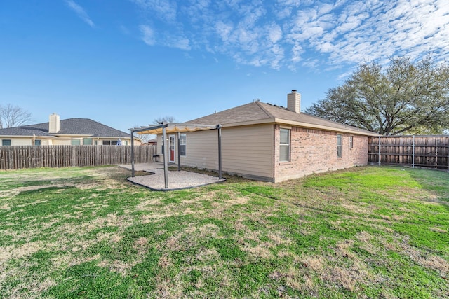 back of house featuring a yard, a fenced backyard, a chimney, a patio area, and brick siding