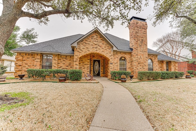 view of front of property with a front lawn, brick siding, roof with shingles, and a chimney