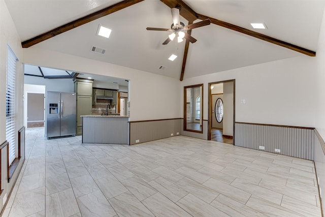 unfurnished living room with visible vents, beam ceiling, a sink, wainscoting, and ceiling fan