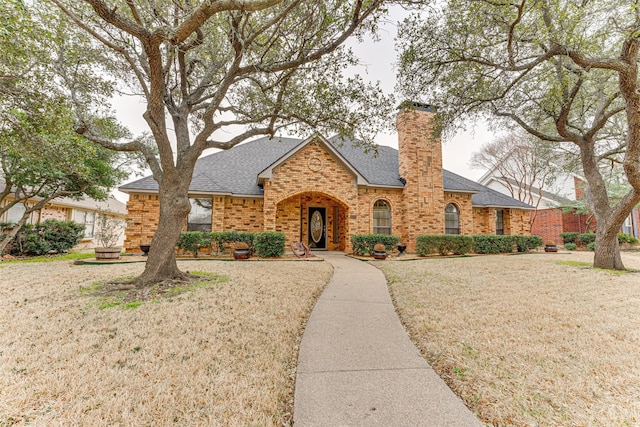 view of front of home with a front yard, brick siding, a chimney, and a shingled roof