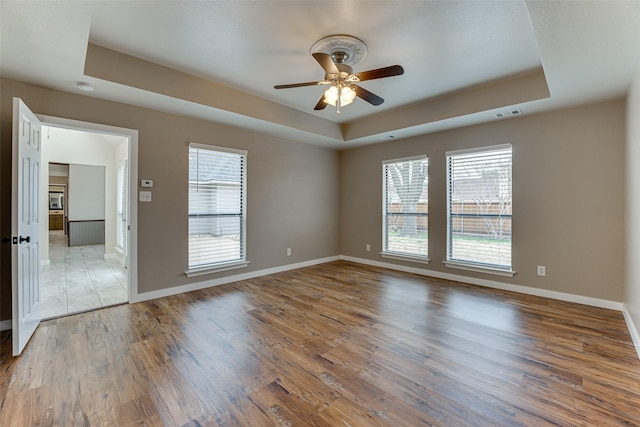 spare room with visible vents, baseboards, light wood finished floors, a tray ceiling, and ceiling fan