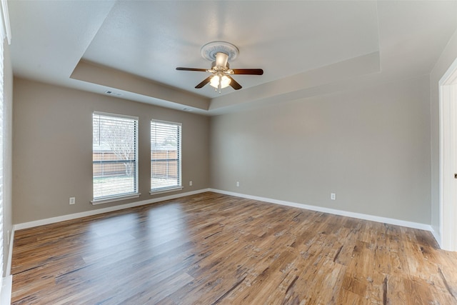 empty room featuring a raised ceiling, baseboards, and wood finished floors