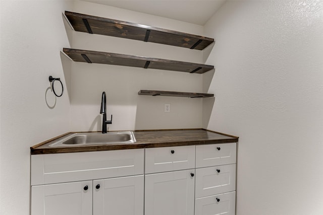 kitchen with wooden counters, open shelves, white cabinetry, and a sink