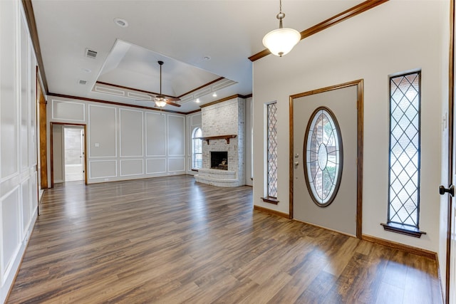 foyer entrance featuring visible vents, a brick fireplace, crown molding, and a decorative wall