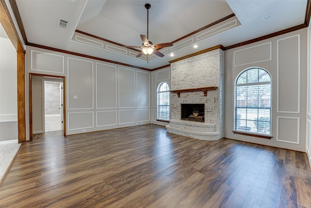 unfurnished living room with a tray ceiling, visible vents, crown molding, and a decorative wall