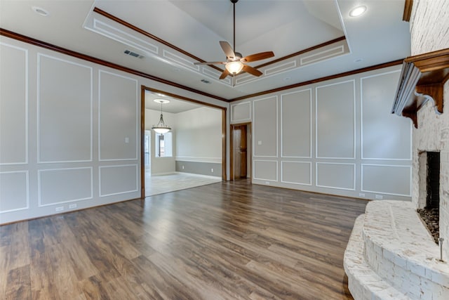 unfurnished living room with a decorative wall, a brick fireplace, a raised ceiling, and ornamental molding