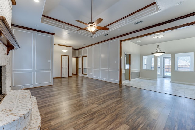 unfurnished living room featuring visible vents, a fireplace with raised hearth, dark wood-style flooring, ornamental molding, and a raised ceiling