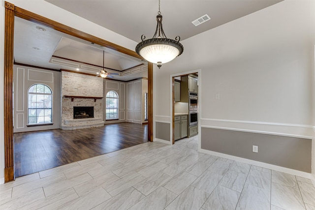 unfurnished living room featuring visible vents, a brick fireplace, baseboards, ceiling fan, and a raised ceiling