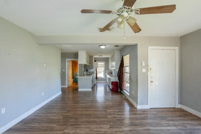 unfurnished living room featuring dark wood-style floors, ceiling fan, and baseboards