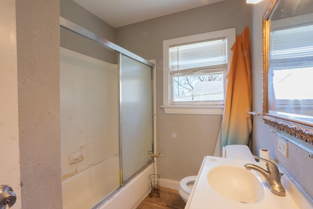 full bath featuring toilet, a sink, enclosed tub / shower combo, wood finished floors, and baseboards