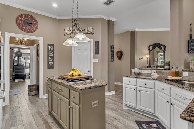 kitchen with visible vents, a kitchen island, ornamental molding, and light wood-style flooring