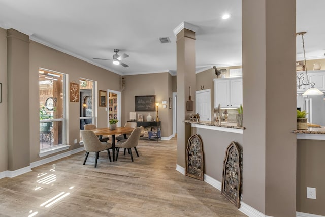 dining space featuring a ceiling fan, crown molding, decorative columns, and light wood-style floors