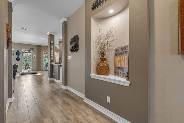 hall with visible vents, decorative columns, wood finished floors, and baseboards