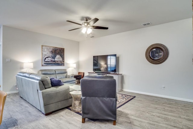 living room featuring a ceiling fan, visible vents, light wood finished floors, and baseboards