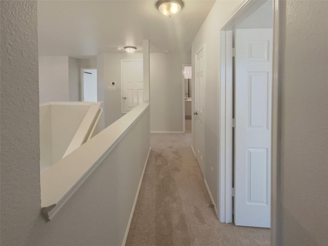 corridor with an upstairs landing, baseboards, and carpet floors