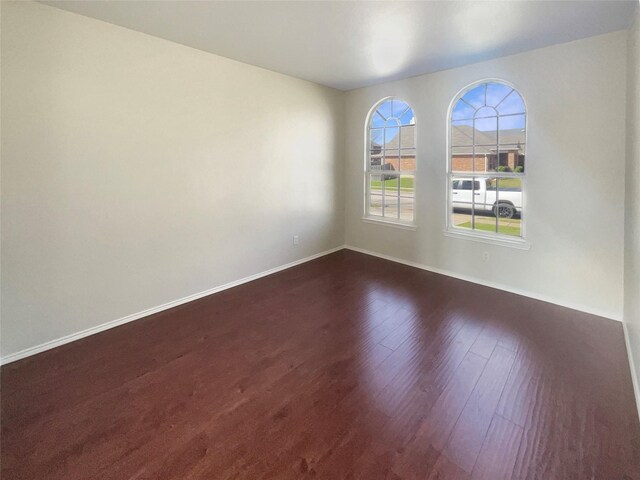 unfurnished room featuring baseboards and dark wood-style flooring