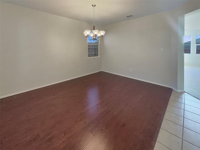 empty room featuring visible vents, baseboards, a notable chandelier, and wood finished floors