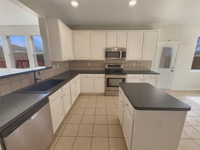 kitchen with light tile patterned flooring, stainless steel appliances, dark countertops, and a sink