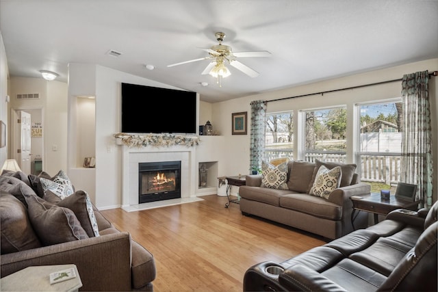 living area with light wood-style floors, a ceiling fan, visible vents, a tiled fireplace, and lofted ceiling