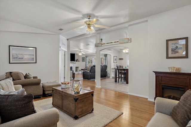 living room with arched walkways, light wood-type flooring, a ceiling fan, a fireplace, and lofted ceiling