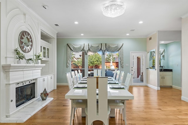 dining space featuring visible vents, baseboards, a fireplace, ornamental molding, and light wood-type flooring