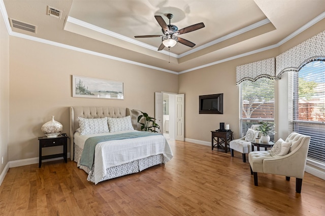 bedroom with a tray ceiling, wood finished floors, and visible vents