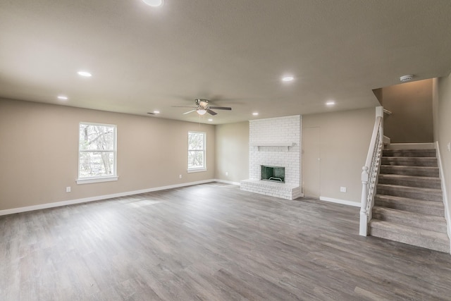 unfurnished living room with baseboards, dark wood finished floors, ceiling fan, stairs, and a brick fireplace