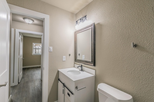 half bath featuring toilet, vanity, and a textured wall