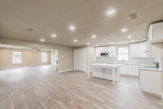 kitchen featuring visible vents, stainless steel microwave, open floor plan, backsplash, and a center island