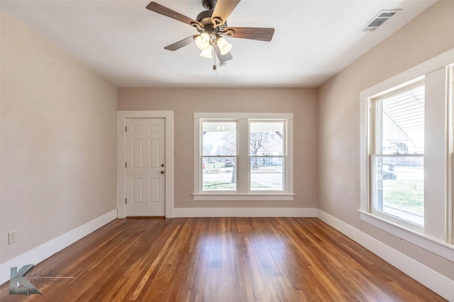 empty room with a wealth of natural light, visible vents, baseboards, and wood finished floors