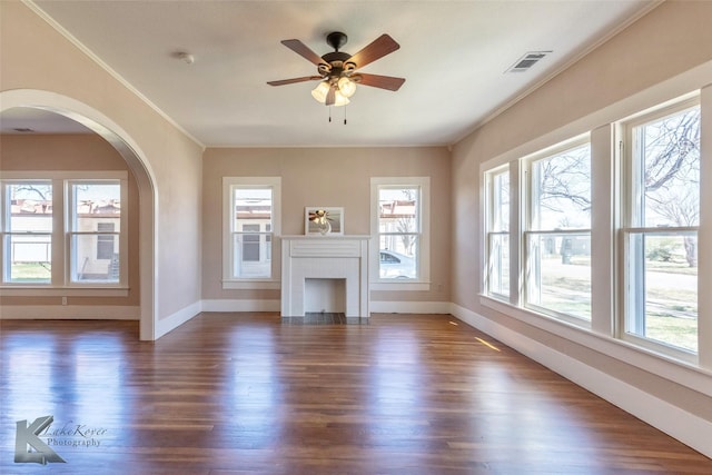 unfurnished living room with a brick fireplace, dark wood-style floors, a wealth of natural light, and ornamental molding